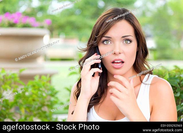 Shocked Young Adult Female Talking on Cell Phone Outdoors on Bench