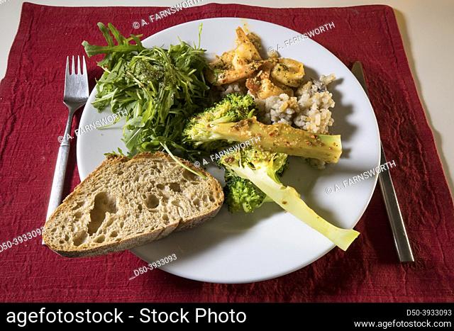 A dinner plate with broccoli, risotto, shrimp , salad and bread