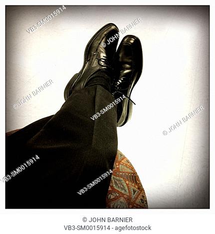Crossed legs with black dress shoes and pants put up onto a footstool