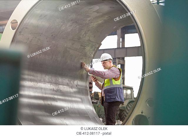 Male engineer examining large steel cylinder in factory