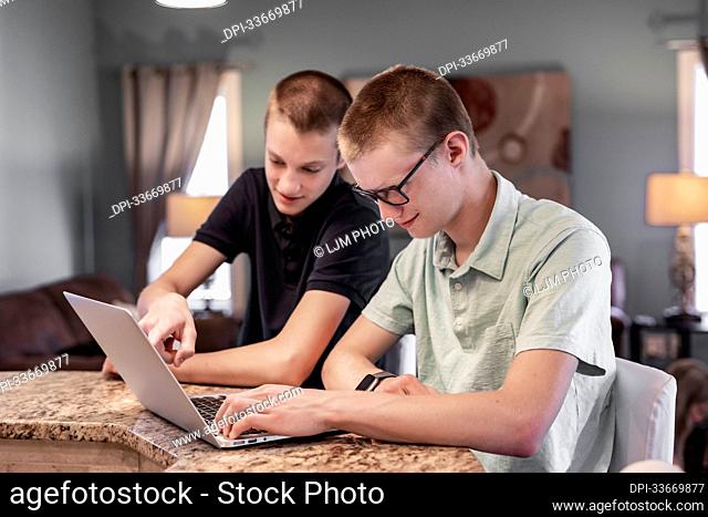 Young man uses a laptop computer at home with his brother assisting him; Edmonton, Alberta, Canada