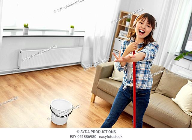 asian woman or housewife with mop singing at home
