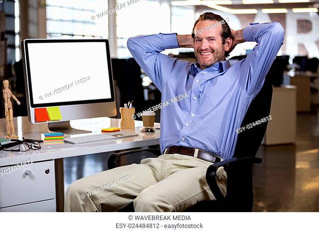 Businessman sitting with hands behind head by desk