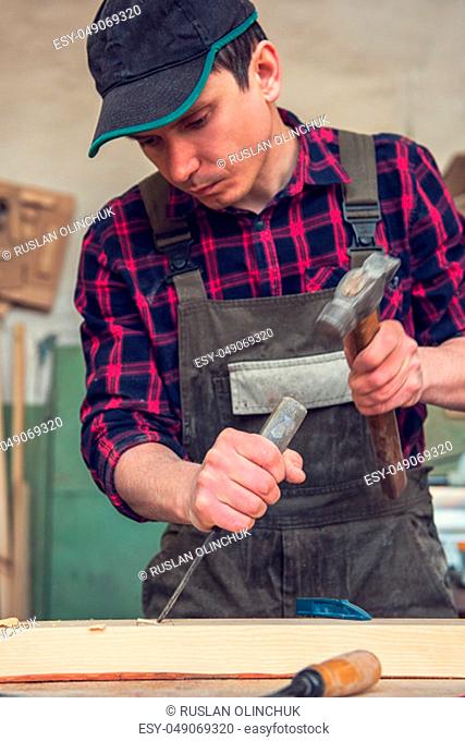 Carpenter working with a chisel and hammer in a wooden workshop. Profession, carpentry and manual woodwork concept