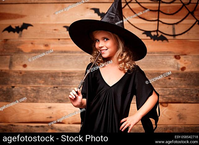 Halloween Witch concept - little witch child enjoy playing with magic wand. over bat and spider web background