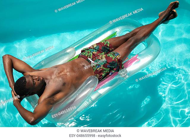 Young African American man with hands behind head relaxing on pool lounger