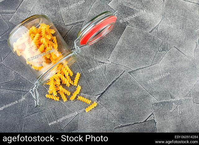 Different uncooked pasta in glass jar on table on dark background