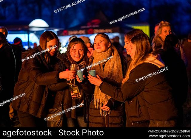 08 April 2023, Brandenburg, Cottbus: Visitors toast each other while watching the Branitz Easter fire. The comrades of the volunteer fire department of the...
