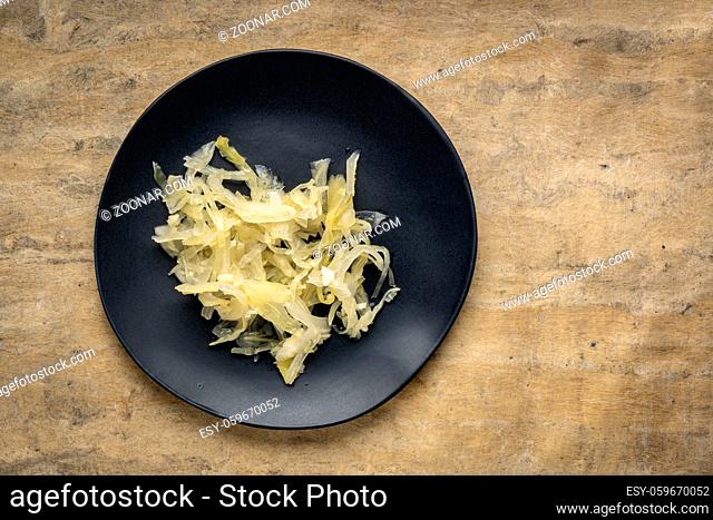 black plate of sauerkraut against bark textured paper background, probiotics concept - fermented food good for gut health