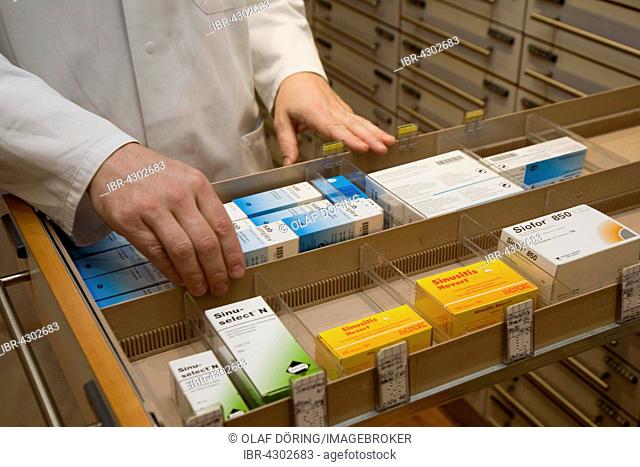 Apotheker taking medication from cabinet in a pharmacy, Germany