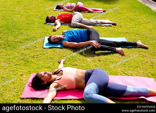 Women and men practicing yoga while lying on exercise mat in park