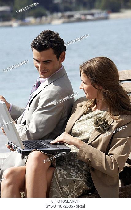 Business couple on beach with fishing rod and laptop