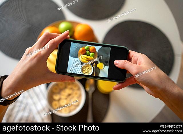 Woman taking photo through smart phone of breakfast on table at home