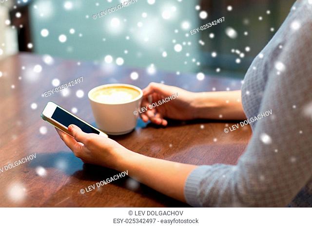 drinks, people, technology and communication concept - young woman with smartphone drinking coffee at cafe over snow