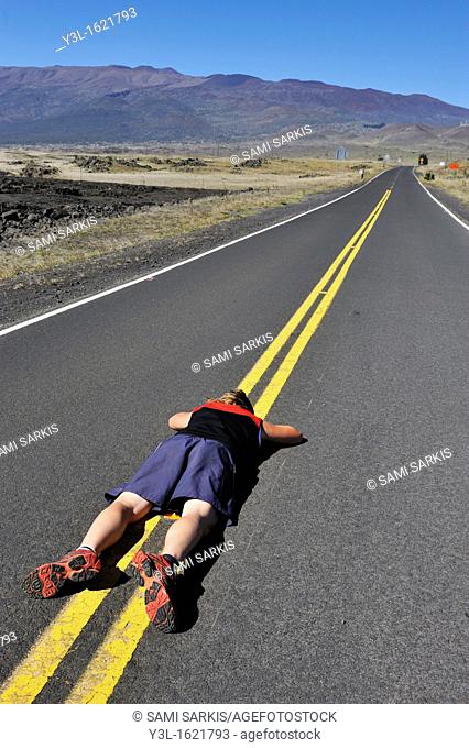 Woman lying down on the road dividing line, Mauna Kea Volcano, Big Island, Hawaii Islands, USA