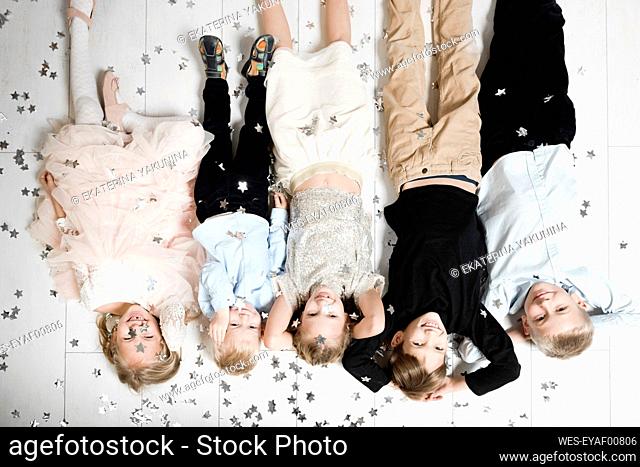 Group picture of five children lying on the floor upside down covered by Christmas confetti