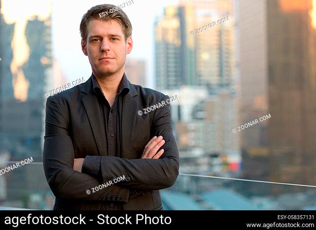 Portrait of young handsome businessman in suit against view of the city
