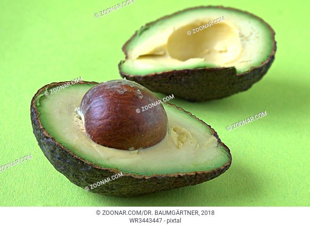 Avocadohälften. Two Avocado halves on green background. The half in the background is blurred