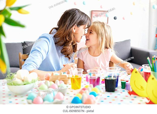 Woman and daughter nose to nose while painting easter eggs at table