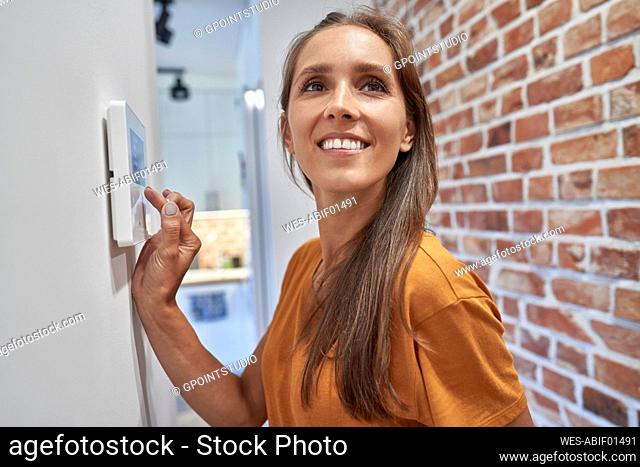 Smiling woman contemplating while using home automation device on wall