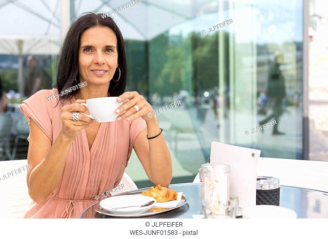 Portrait of smiling mature woman drinking coffee at pavement cafe