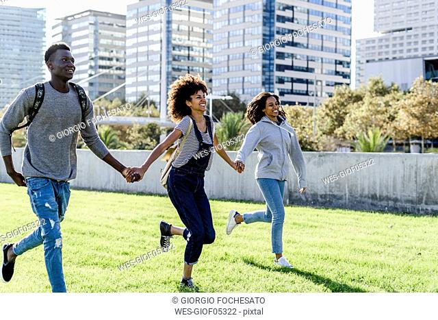 Three friends running on a lawn in the city, laughing