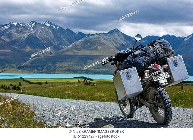 Enduro motorcycle on a gravel road at the glacial Lake Pukaki, with a view to the mountains of the Ben Ohau Range, South Island, New Zealand