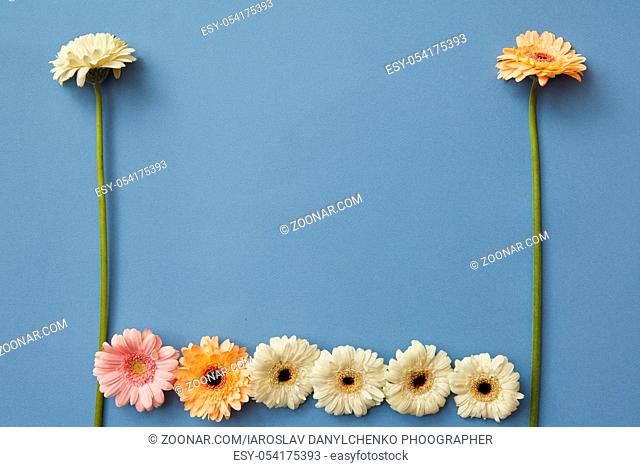 A pattern of white, orange and pink gerberas on a blue paper background. Figures from the game Tetris. Minimal spring concept. Flat lay