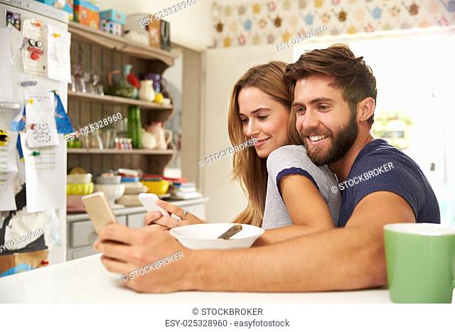 Young Couple Eating Breakfast Whilst Using Mobile Phones