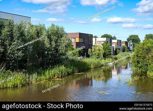 Groningen, The Netherlands - Contemporary country style houses at the waterfront surrounded by nature over blue sky in the suburbs