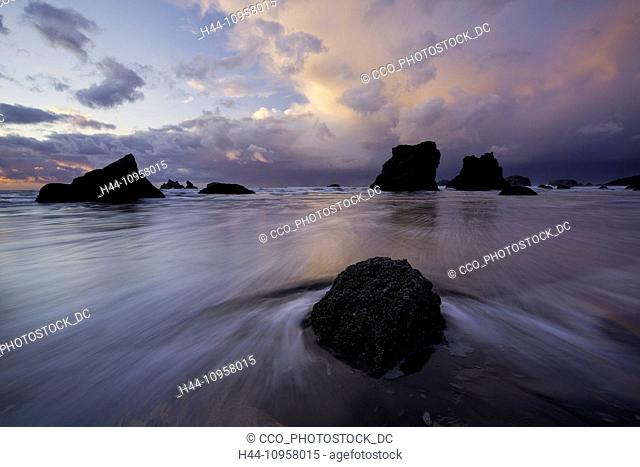 Tidepools, a wave, and sea stacks, rocks, at sunset along Bandon Beach, Oregon. Winter. USA