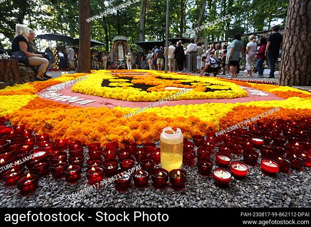 15 August 2023, Bavaria, Ziemetshausen: Pilgrims stand at the pilgrimage site Maria Vesperbild at the Marian grotto, next to a flower carpet lined with candles