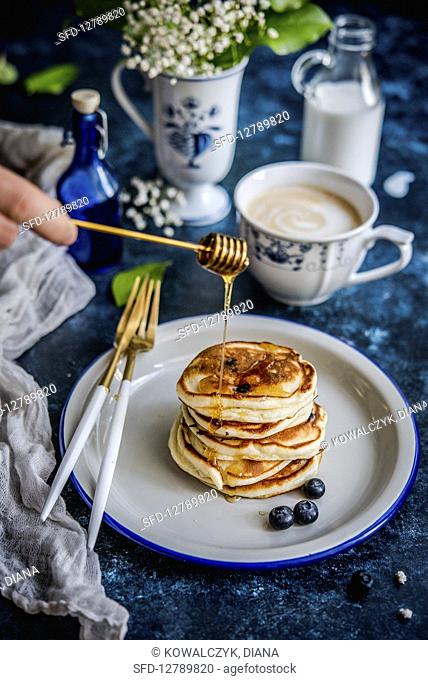 Blueberry pancakes stack with honey, coffee with milk in the background
