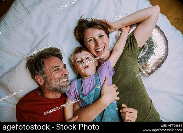 Smiling mother, father and son lying on bed at home
