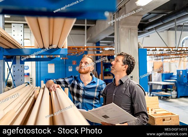 Two carpenters examining wooden poles in production hall