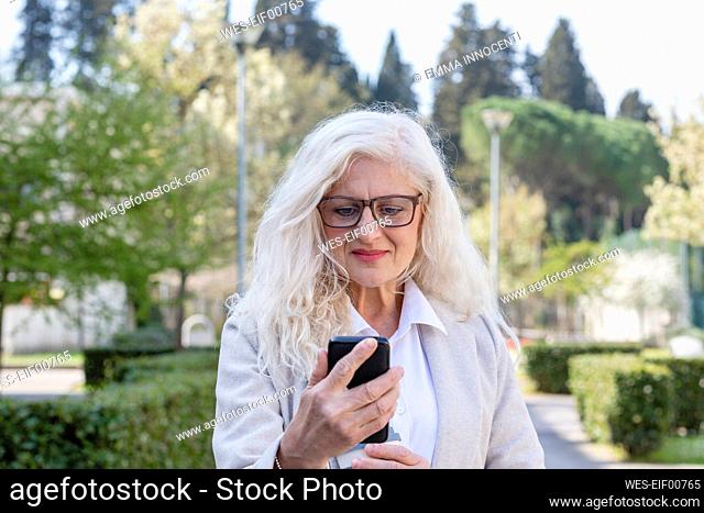Mature woman with long white hair using mobile phone at park