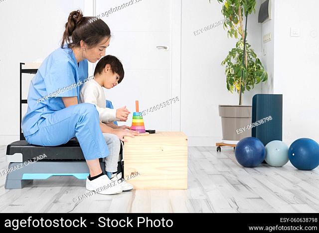 Therapist doing development activities with a little boy with cerebral palsy, having rehabilitation, learning . Training in medical care center