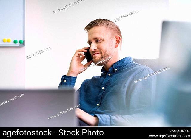 Smiling Businessman Looking Away While Communicating On Mobile Phone In Office