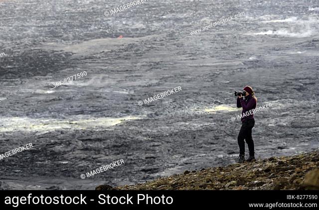 Photographer taking pictures with camera, lava fields in the back, volcanic eruption, active table volcano Fagradalsfjall, Krýsuvík volcano system