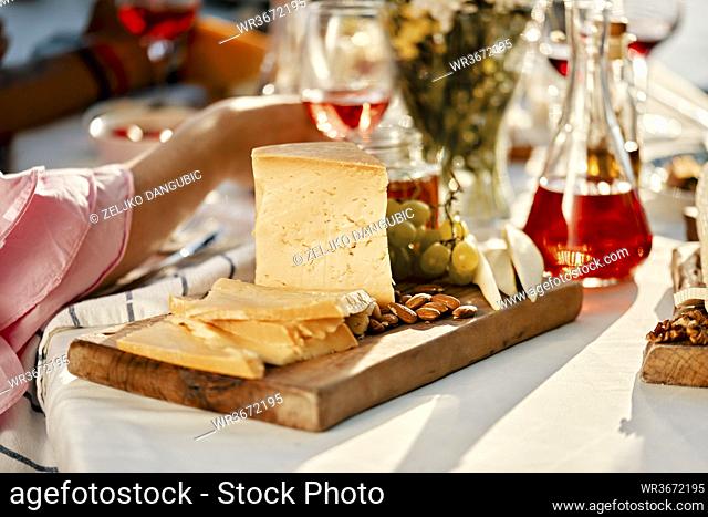 Cheese platter and wine on table with people in background