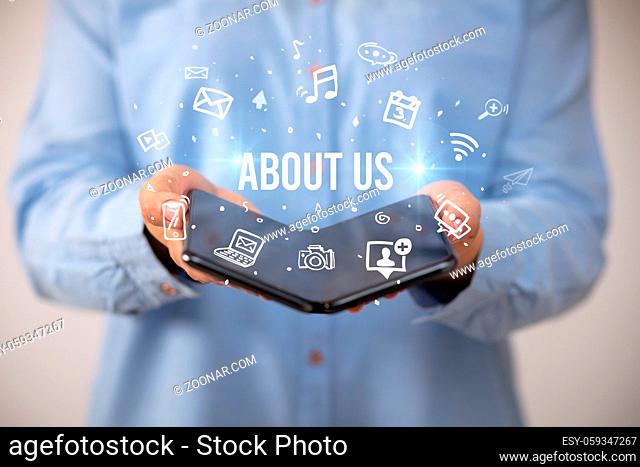 Businessman holding a foldable smartphone with ABOUT US inscription, social media concept