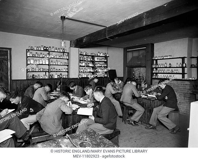 Bembridge School, Hillway Road, Bembridge, Isle Of Wight. Students working at desks in a chemistry classroom. There are shelves containing a variety of bottles...