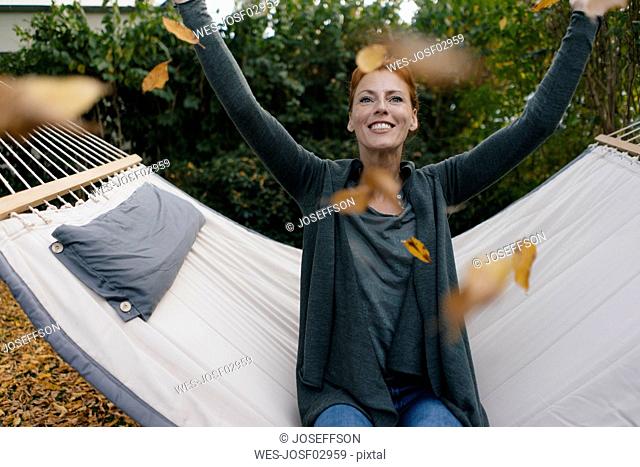 Carefree woman in hammock throwing autumn leaves