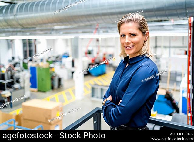 Confident businesswoman wearing blue shirt standing with arms crossed at factory