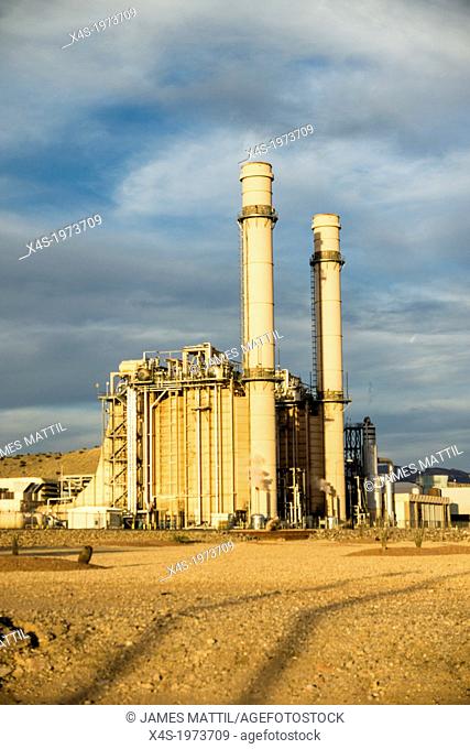 A modern, state-of-the-art gas-fired electric generating station with tall smokestacks in the golden light of sunset