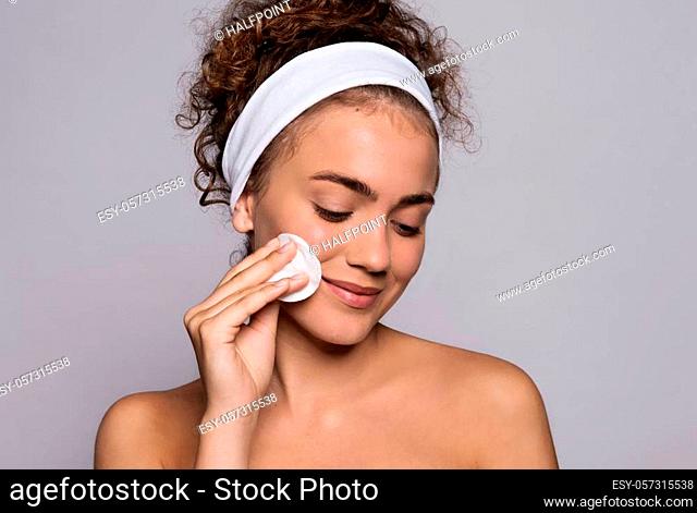 A portrait of a young woman cleaning face with cotton wool in a studio, beauty and skin care