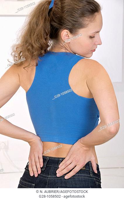 young woman suffering from backache, seen from behind hands holding her back, in blue sports top