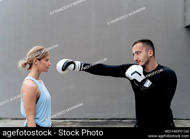 Sportsman practicing boxing with woman while standing against wall