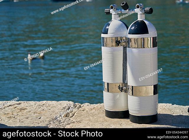 Two white diving tanks leaning against the seashore in a harbour