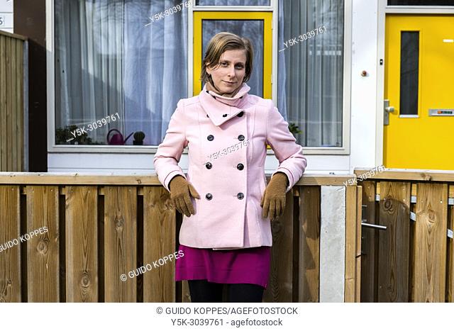 Tilburg, Netherlands. Portrait of a young, caucasian woman, standing proudly in front of her newly aquired apartment at the north side of town